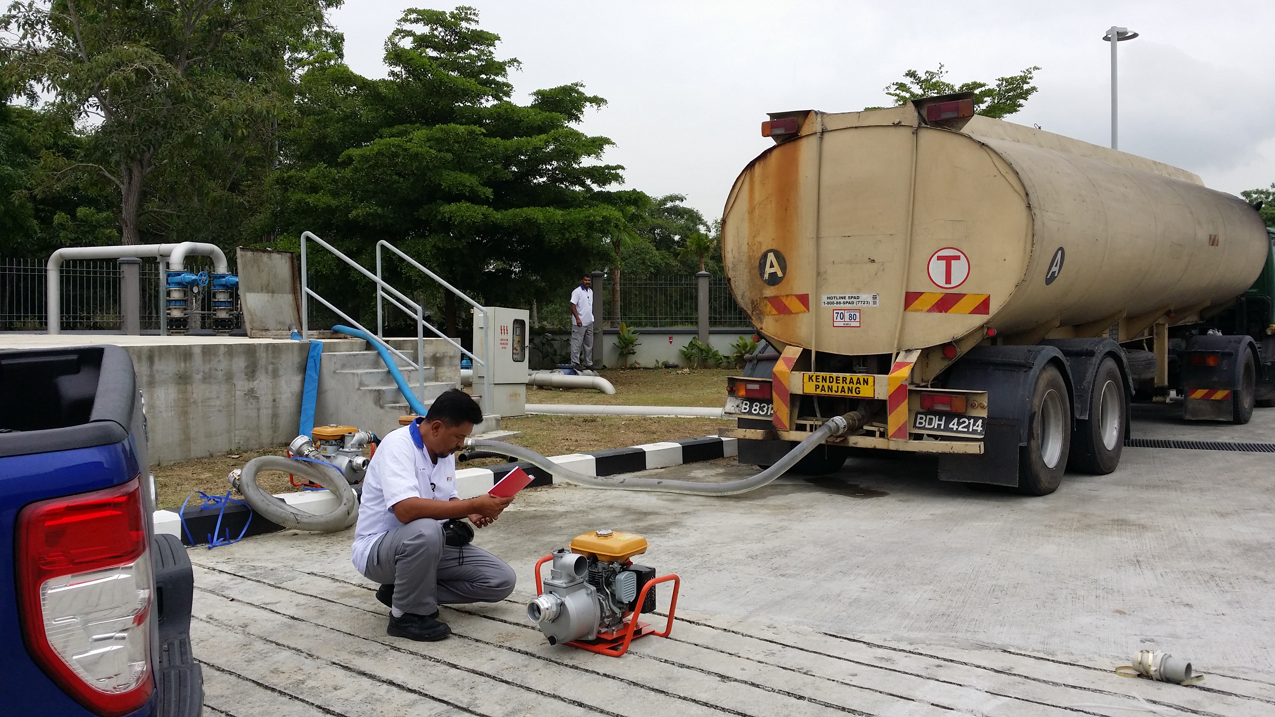 Water tanker, transfer hose and portable pump at an industrial receiving point